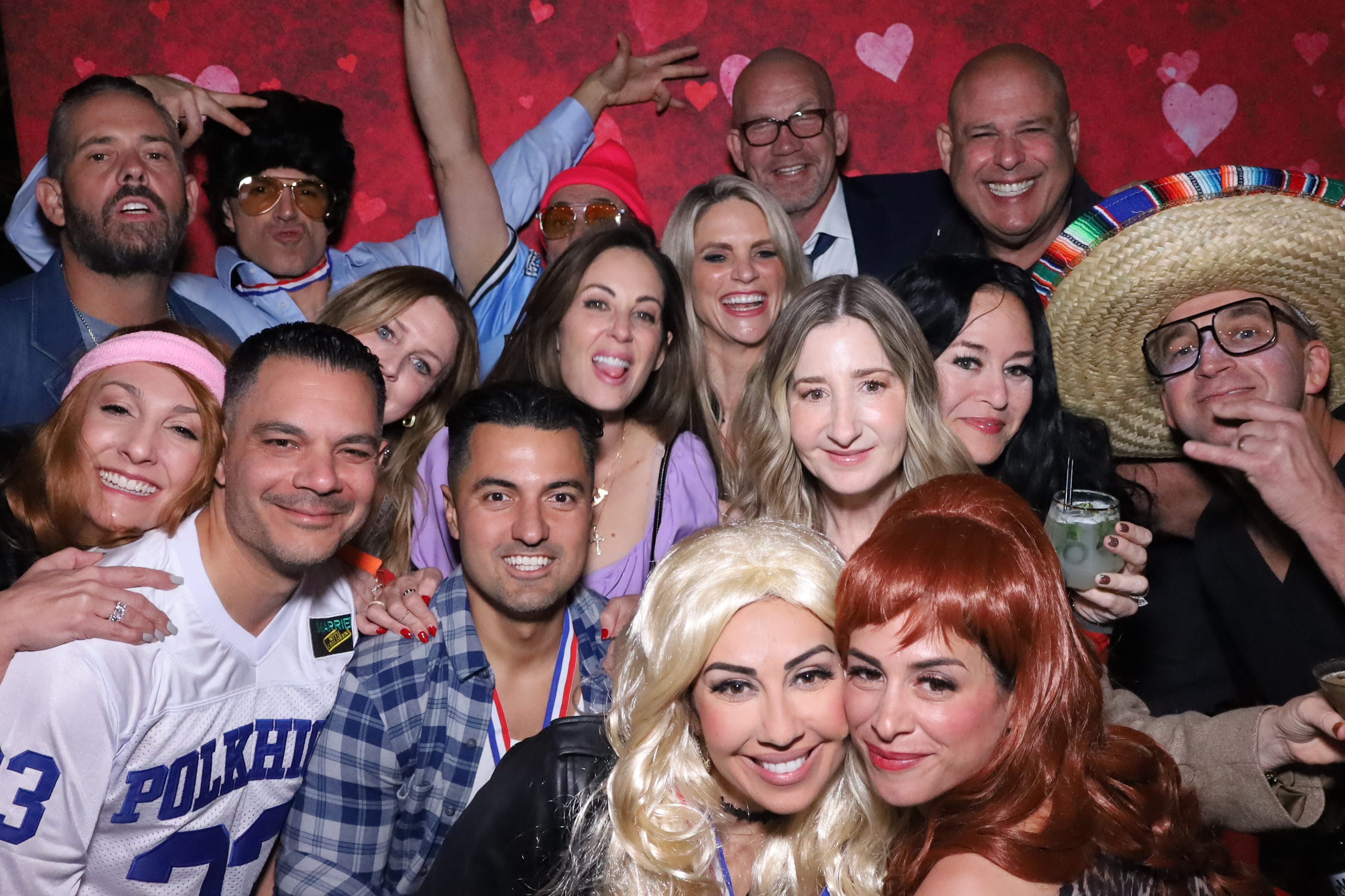 Large group celebrating at the Twinkle Mirror Booth — red Valentine's backdrop with hearts